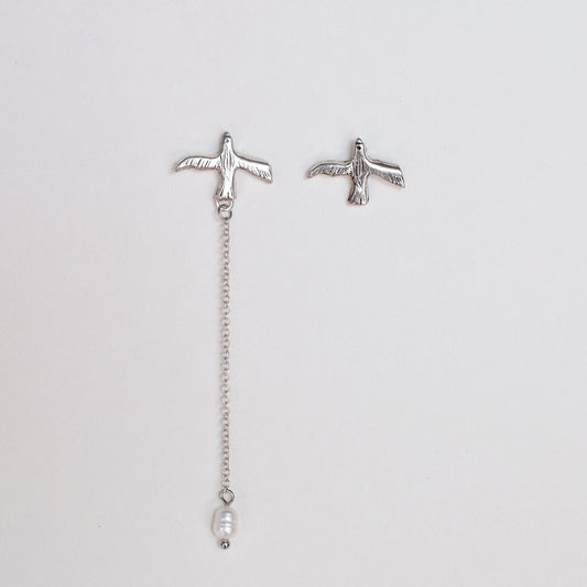 Pair of silver earrings with chain and pearl on a light gray background