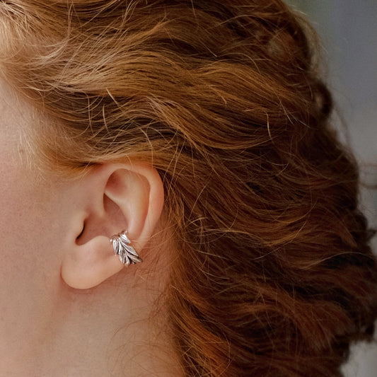 A person with red hair is wearing a silver cuff earring designed with a wheat motif.