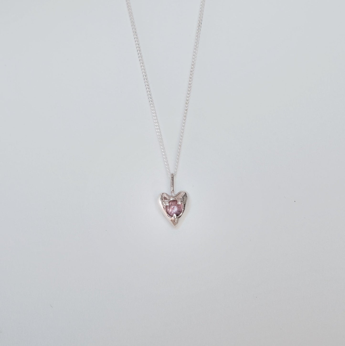 Heart-shaped pink gemstone necklace on a thin chain against a light gray background